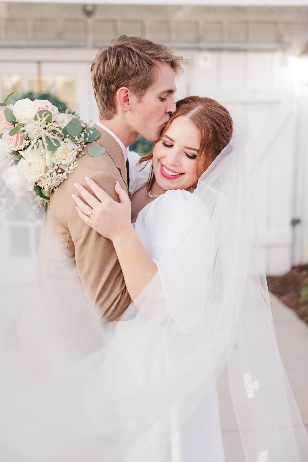 A romantic wedding moment with the couple embracing under soft lighting while a bouquet of white flowers rests nearby.
