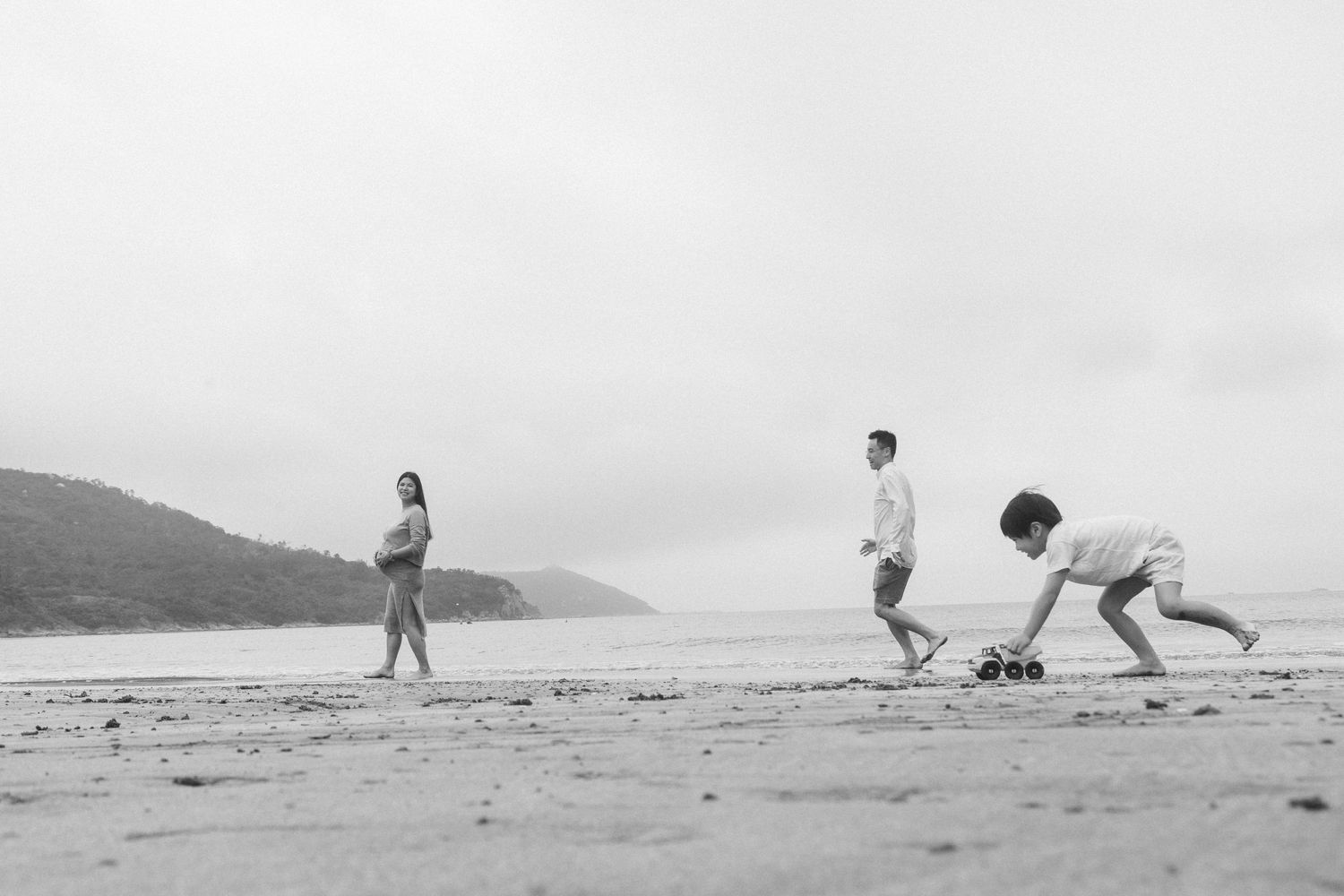 Three people enjoying a playful moment together on a misty beach in black and white.