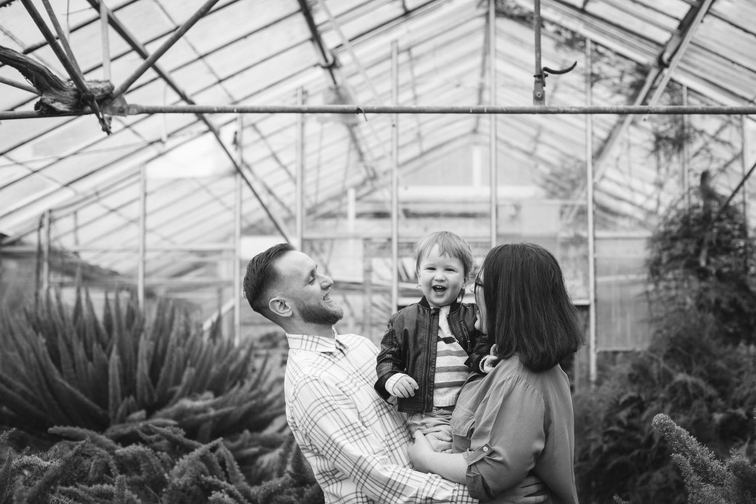 Family sharing cheerful moment together inside plant-filled greenhouse.