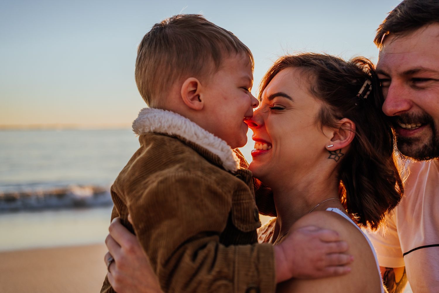 a boy kissing his mothers nose with the father standing behind