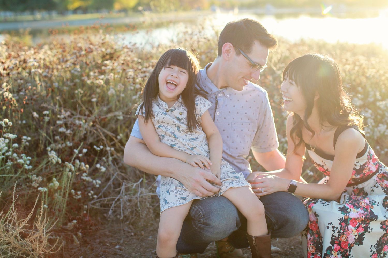 Family enjoying playful moment together in sunlit field with wildflowers.