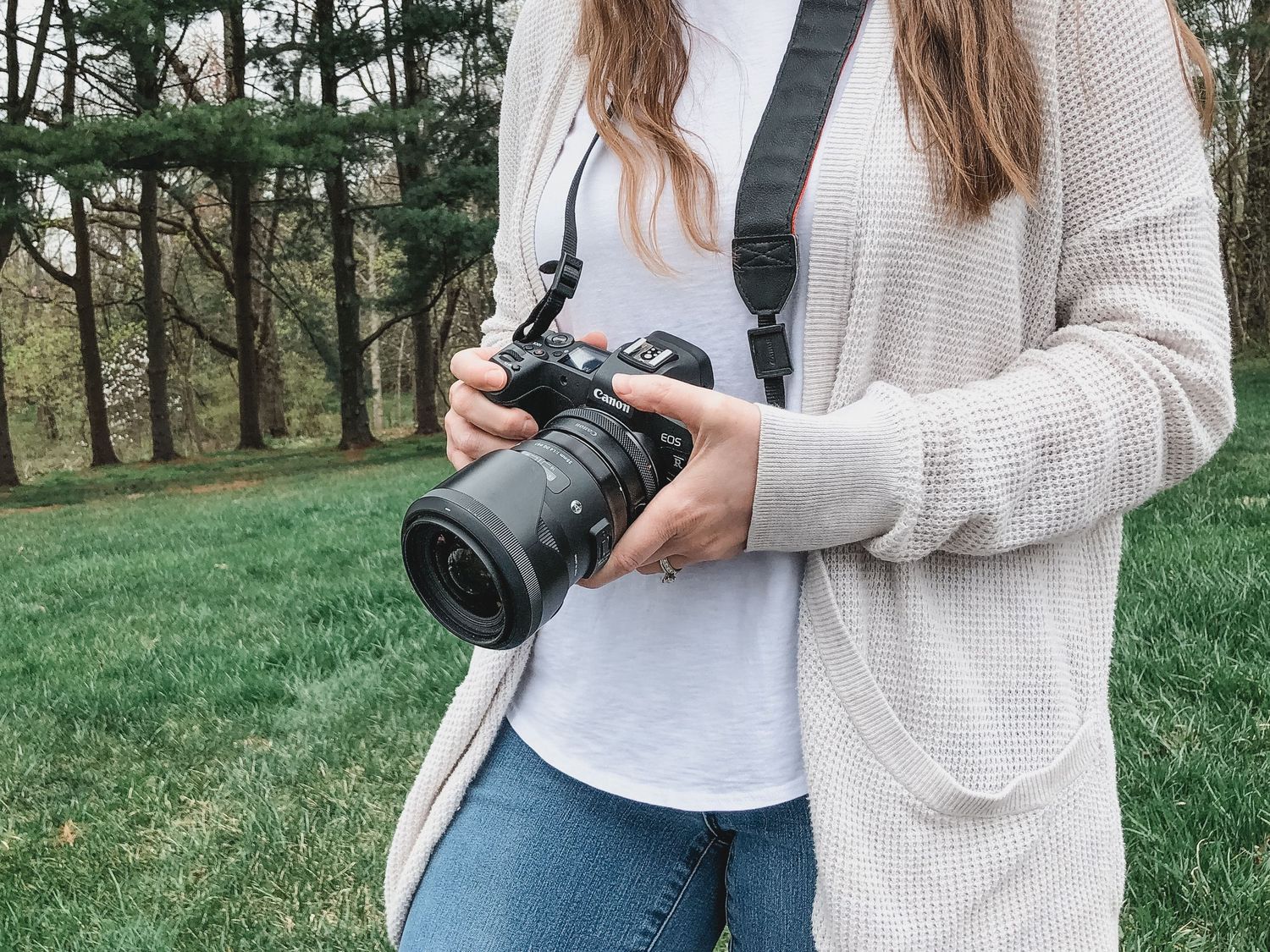 Person in a cream cardigan holding a professional camera outdoors.
