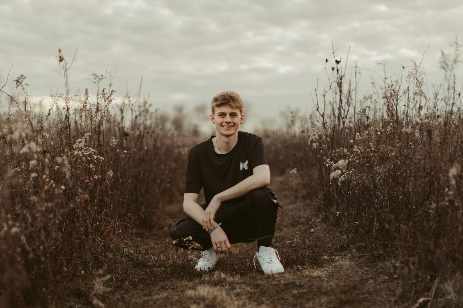 Person in black clothing sitting among tall dried grass during golden hour.