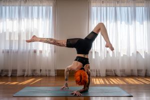 Person performing yoga poses on a blue mat in front of sheer curtains.