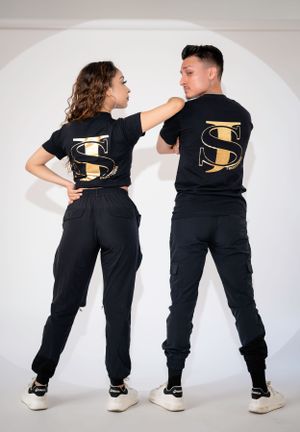 A couple wearing matching black outfits poses playfully against a white background.