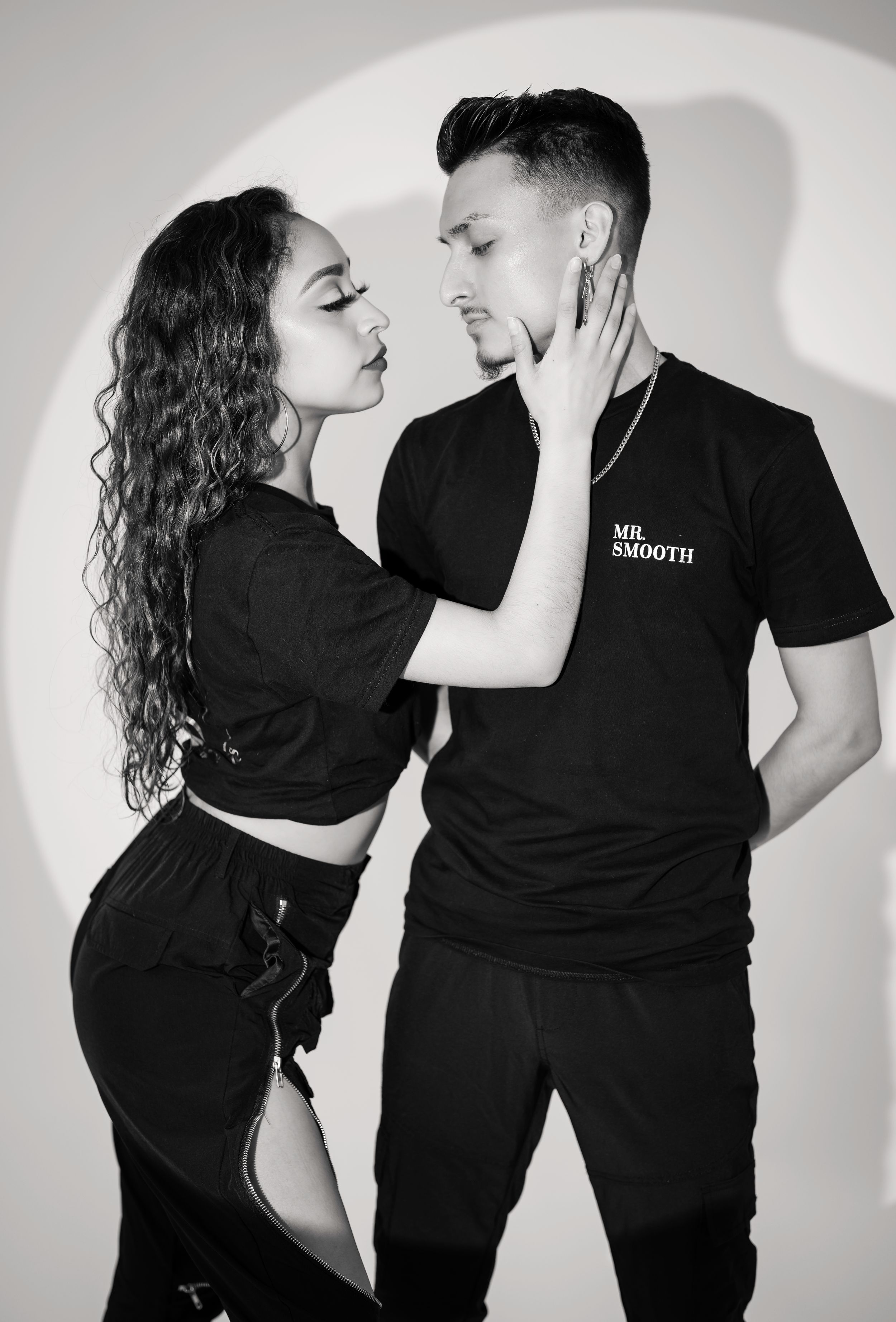 A couple in coordinated black outfits poses for artistic black and white photos.