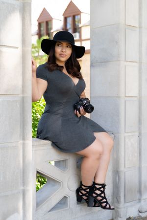 Fashion portrait with black hat and dress against white columns.