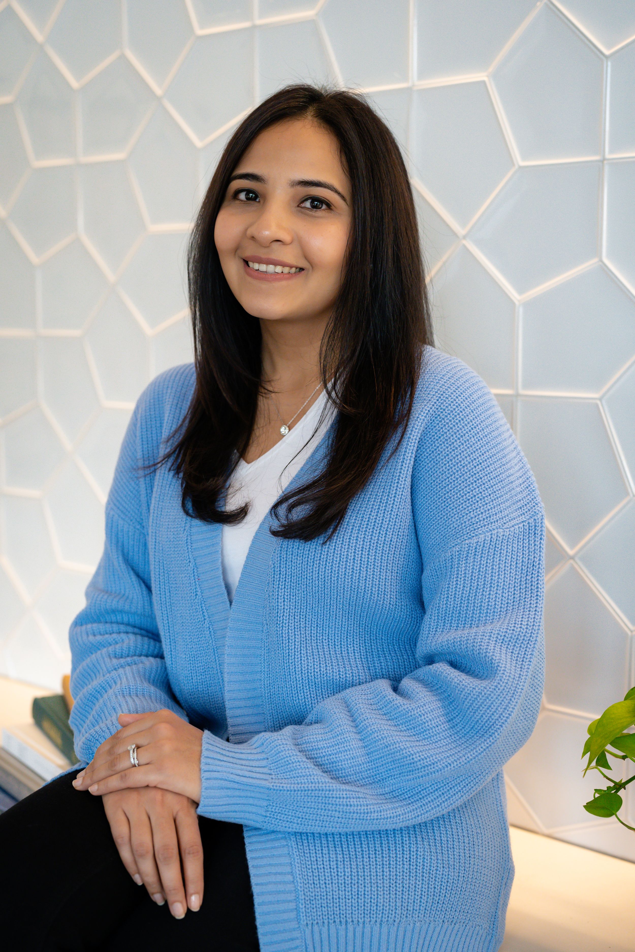 Professional studio portrait of someone wearing a light blue knit sweater against a geometric patterned background.