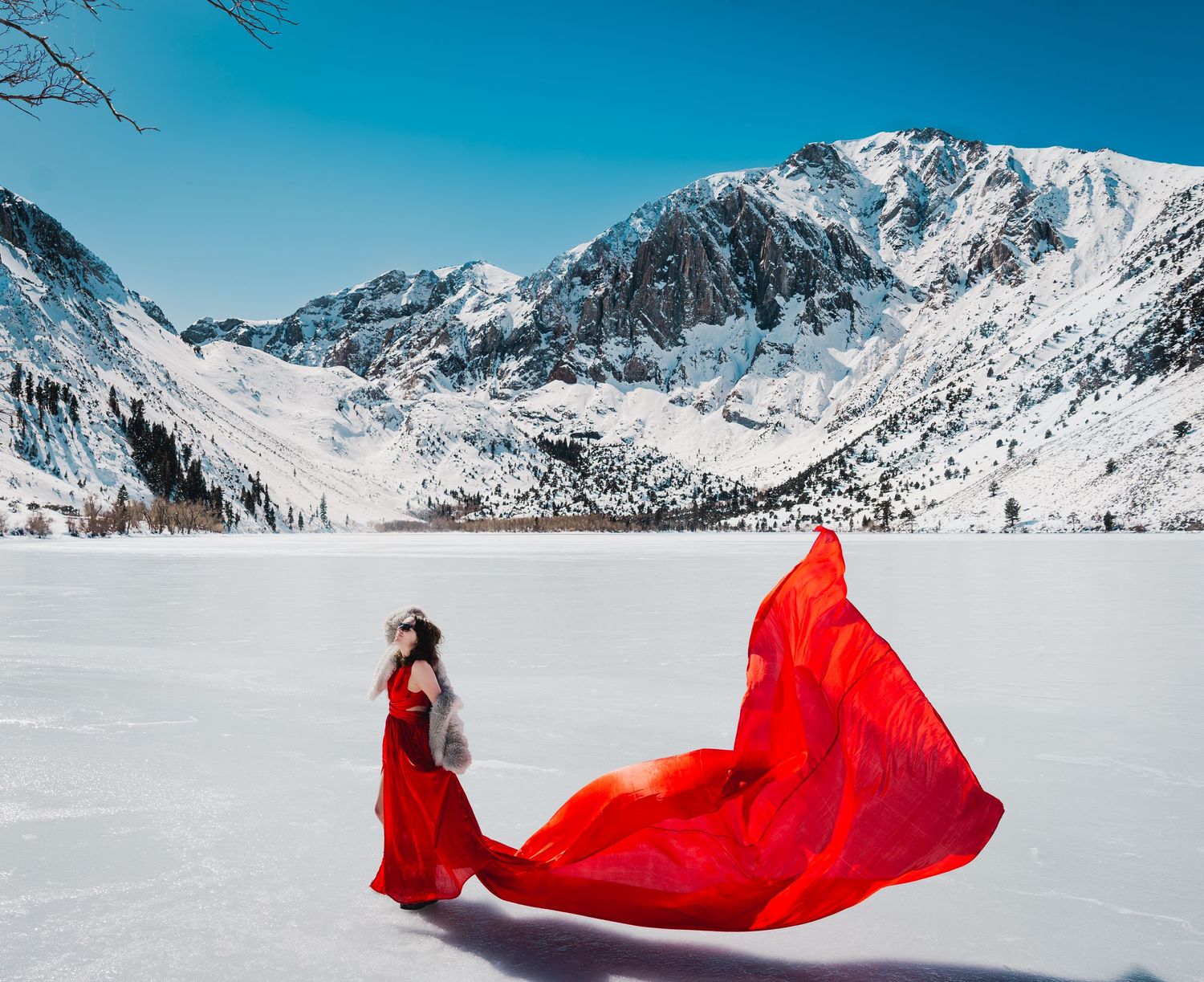 woman on ice of convict lake, mammoth lakes, california wearing a red flying dress.