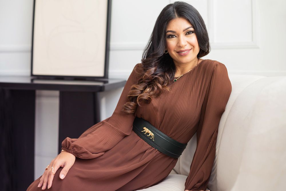 Brunette in brown dress with belt poses elegantly on white couch.