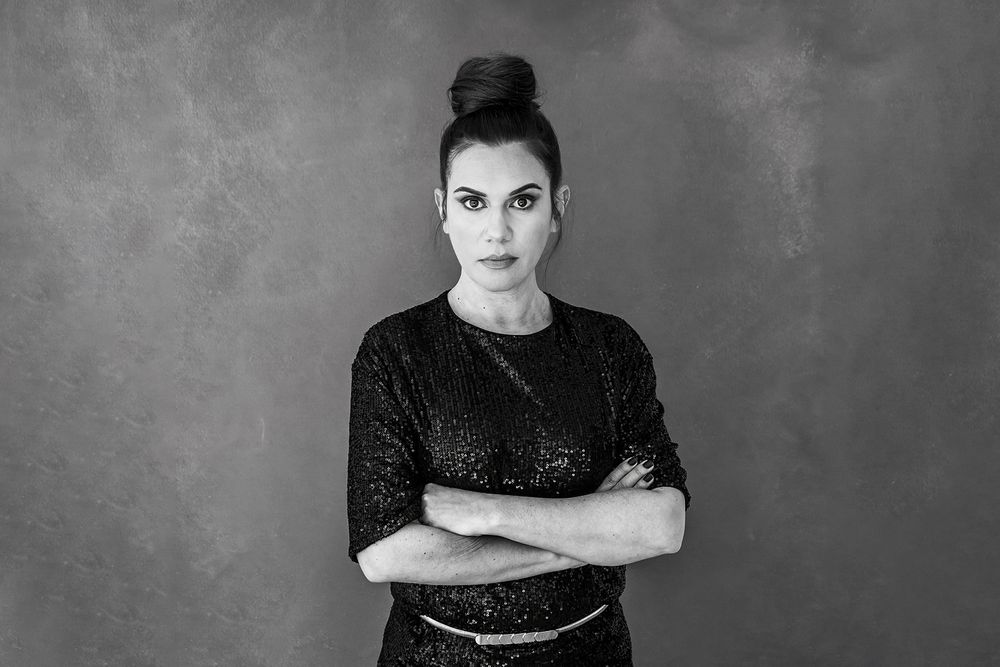 Black and white studio portrait with dramatic lighting and posed stance.