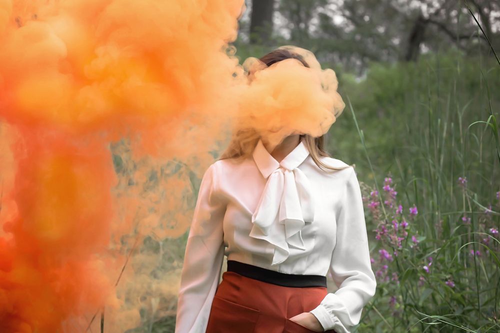 Figure in white blouse with orange smoke effect in nature setting.