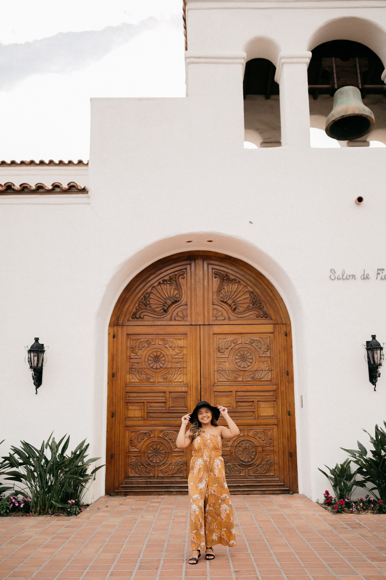 Yellow floral dress worn at Spanish-style building with ornate wooden doors and white stucco walls.