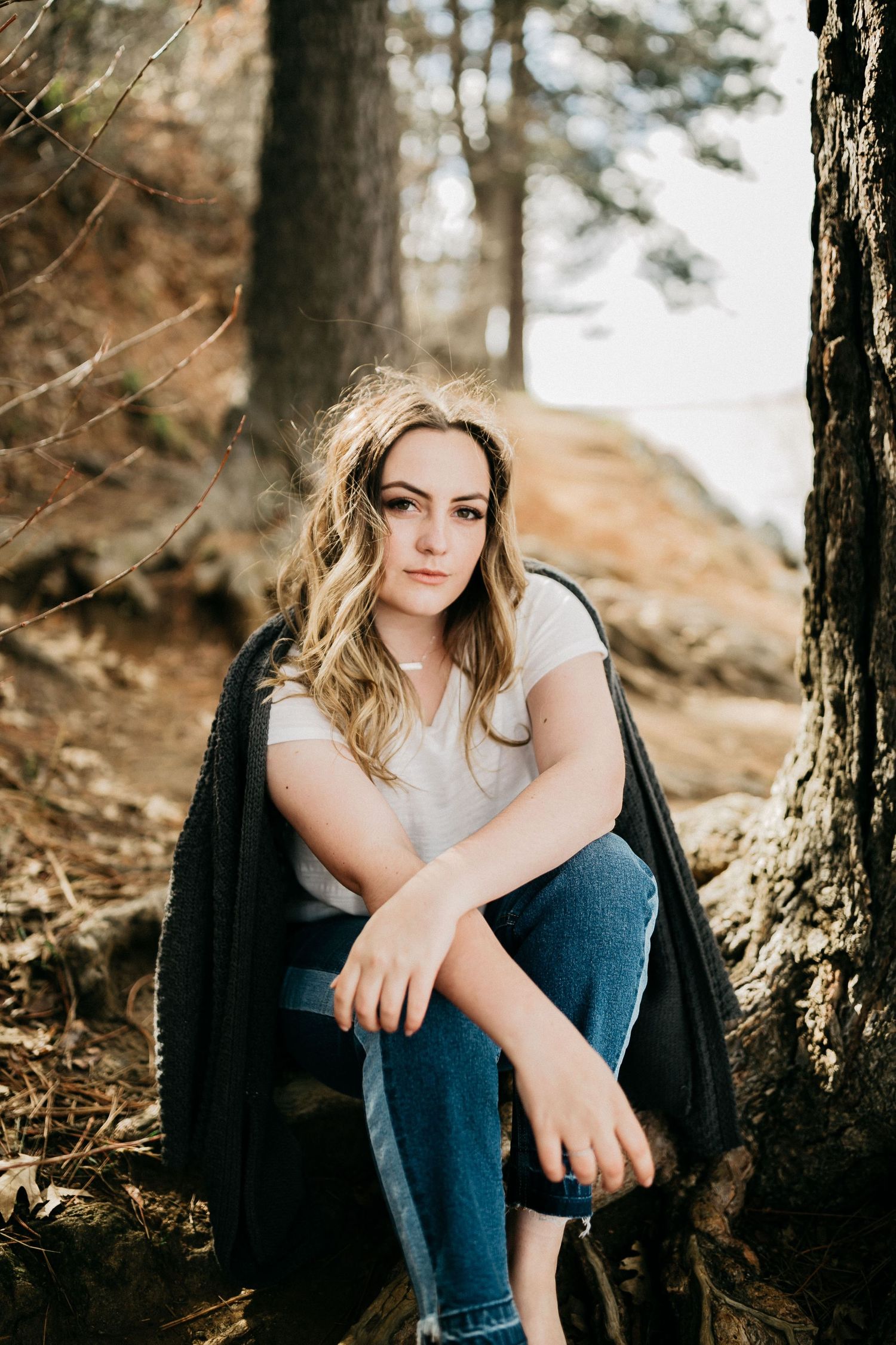 Casual portrait in nature wearing jeans and cardigan while sitting near trees.