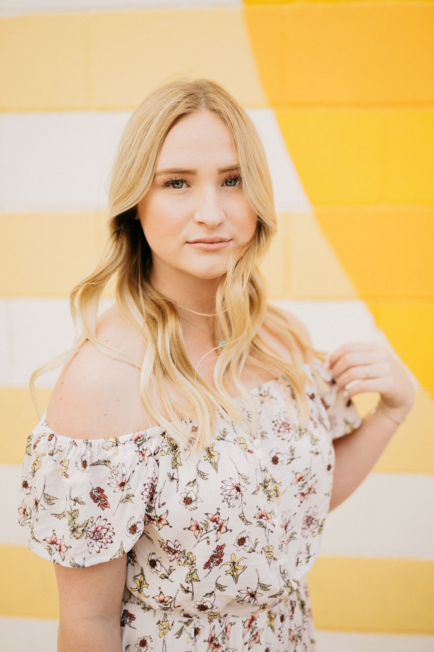 Portrait against yellow and white striped background wearing floral off-shoulder dress.