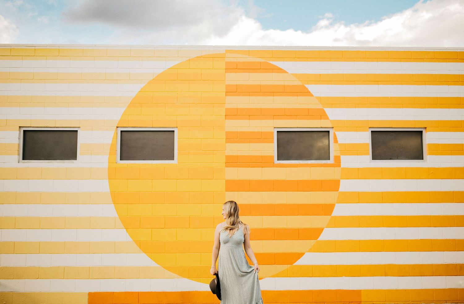Retro-styled yellow striped wall with sun design and figure in dress.