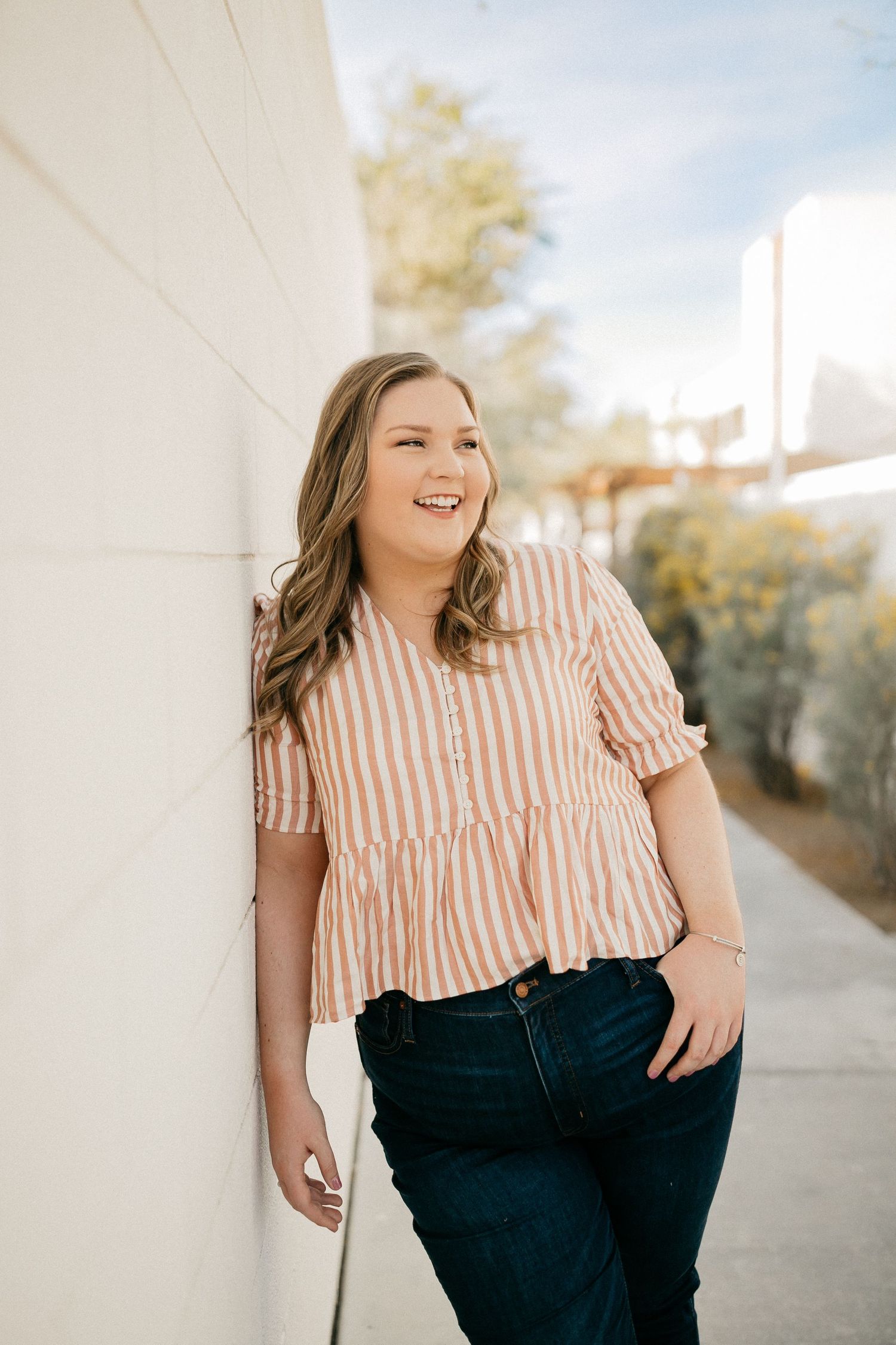 Casual outdoor portrait in striped top and jeans against white wall.