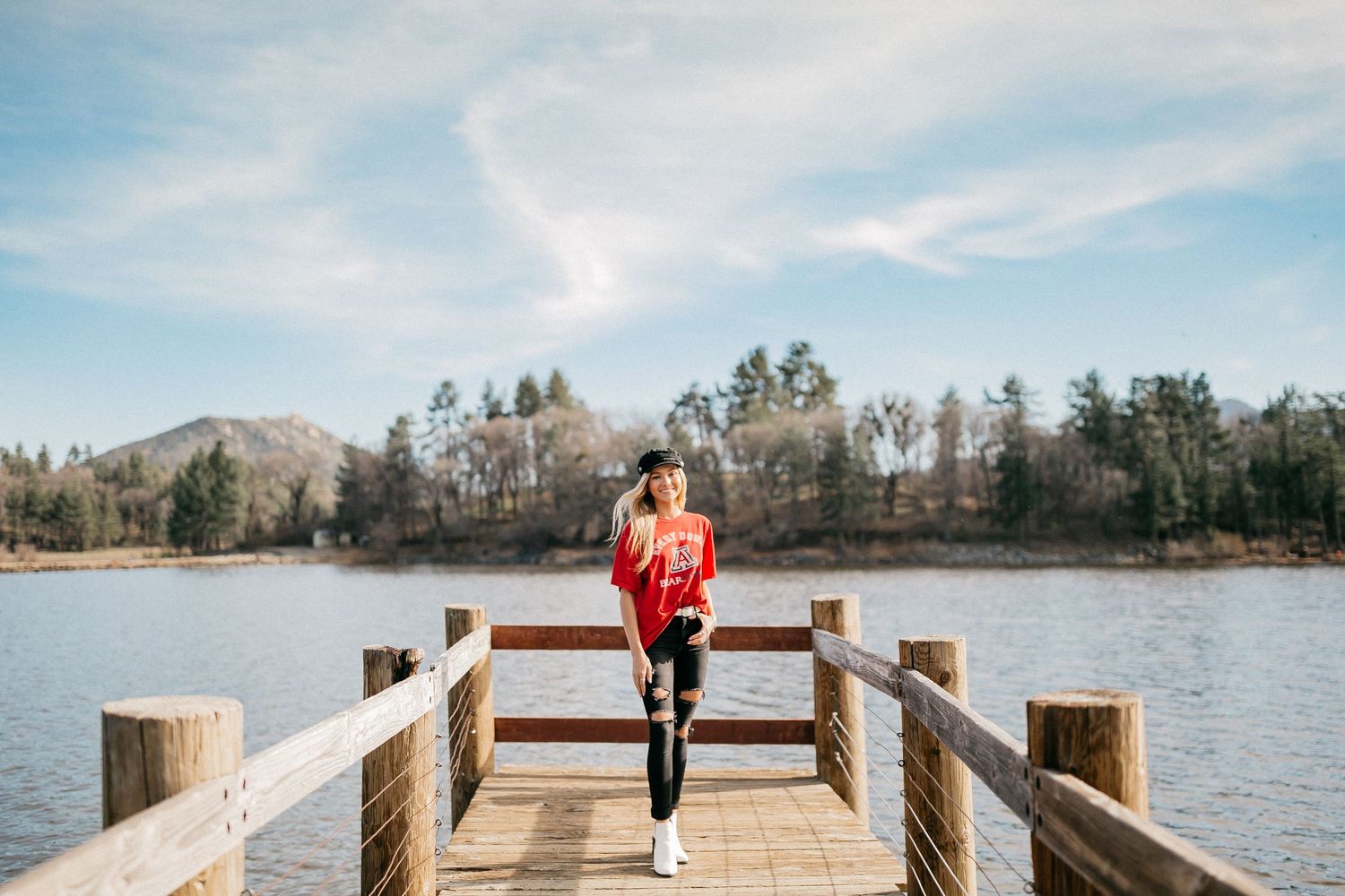Person in red jacket standing on wooden pier overlooking mountain lake.