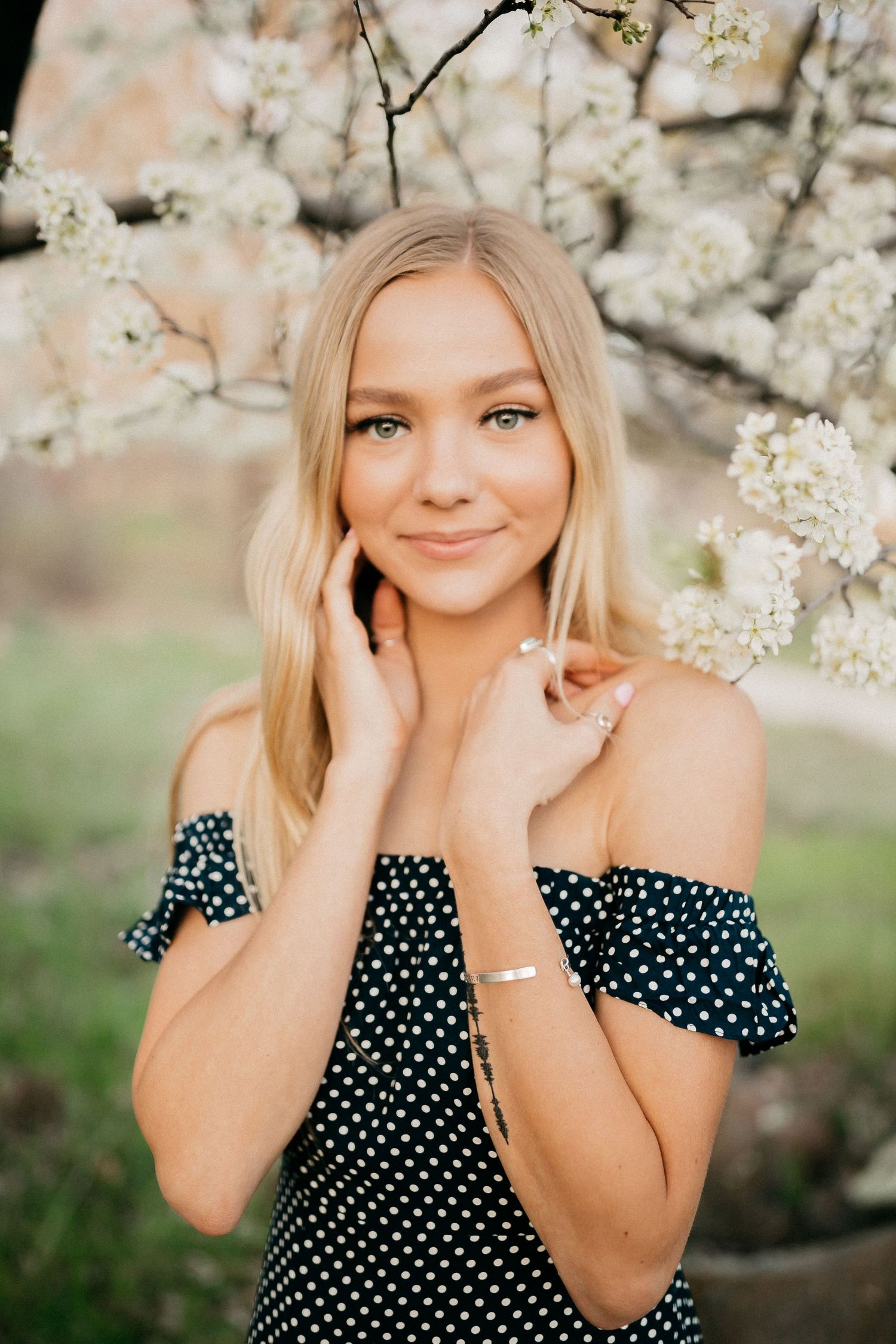 Portrait in spring with blooming white cherry blossoms framing subject in polka dot dress.