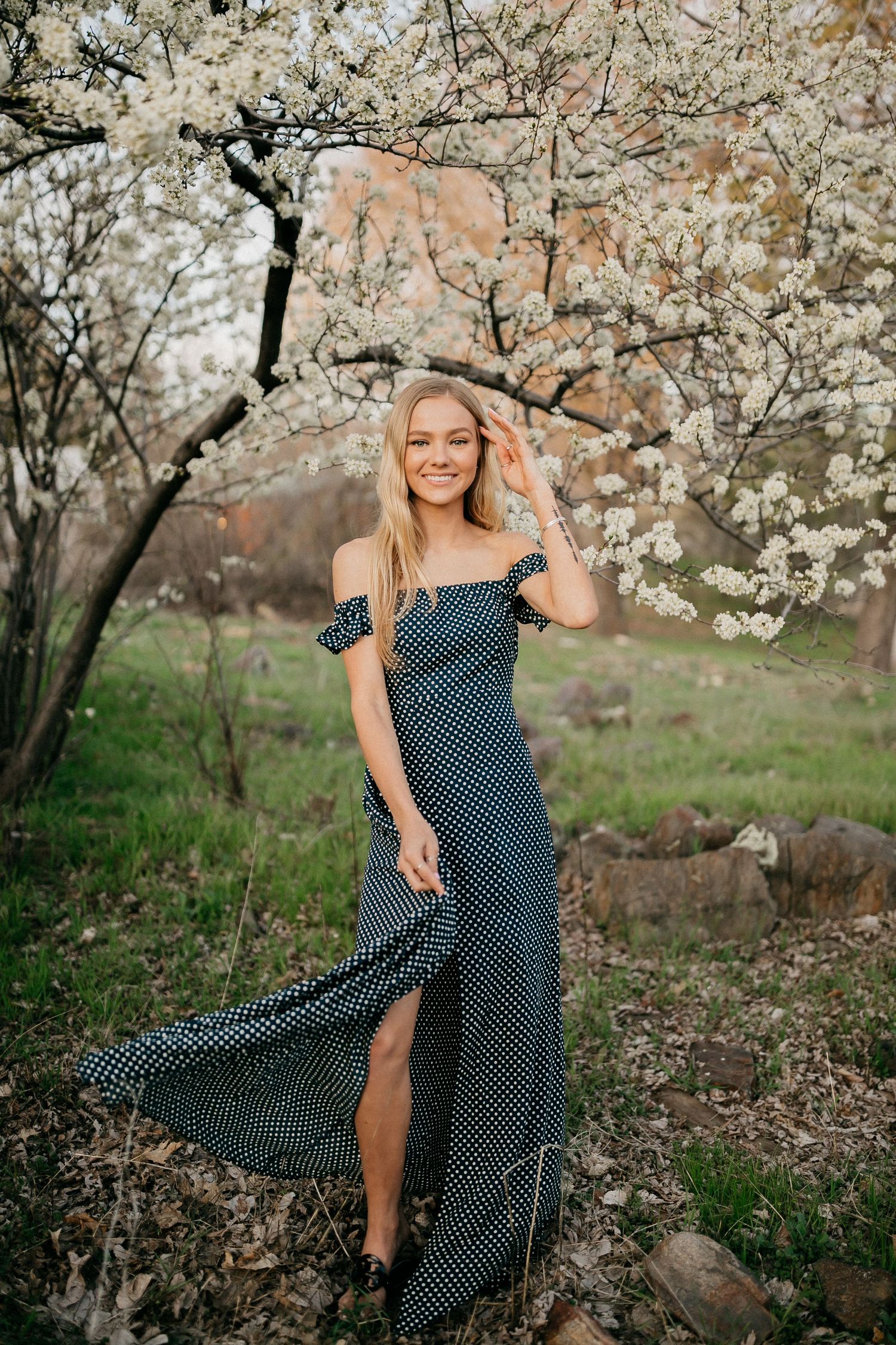 Woman in polka dot dress posing under blooming cherry blossom trees in spring.