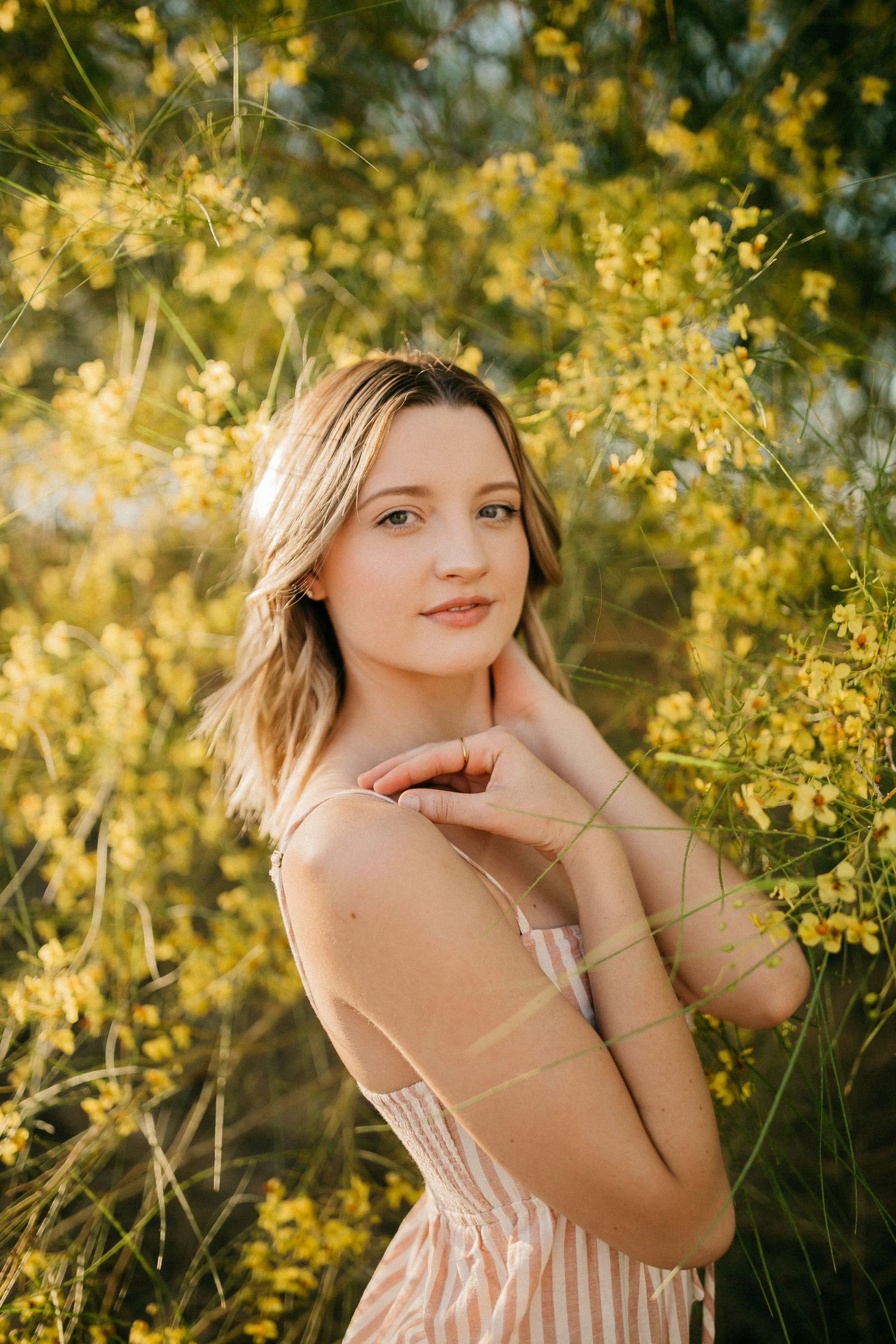Spring portrait among blooming yellow flowers in striped dress.