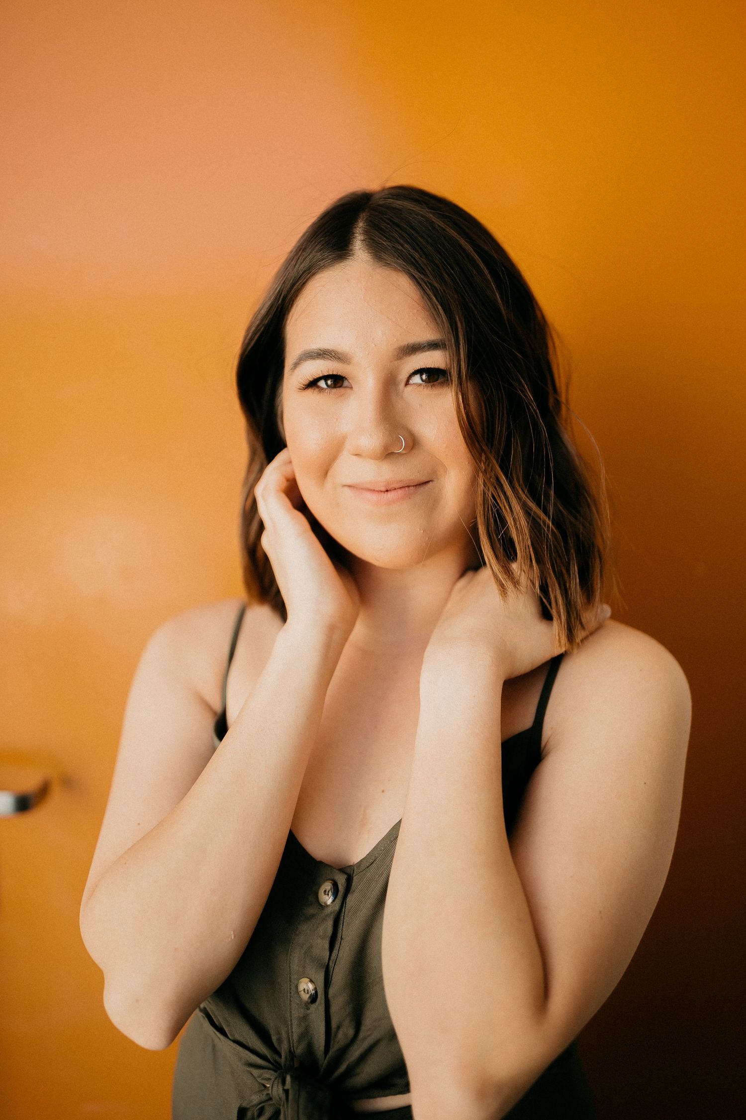 Portrait against orange wall showing warm expression and casual style in dark top.