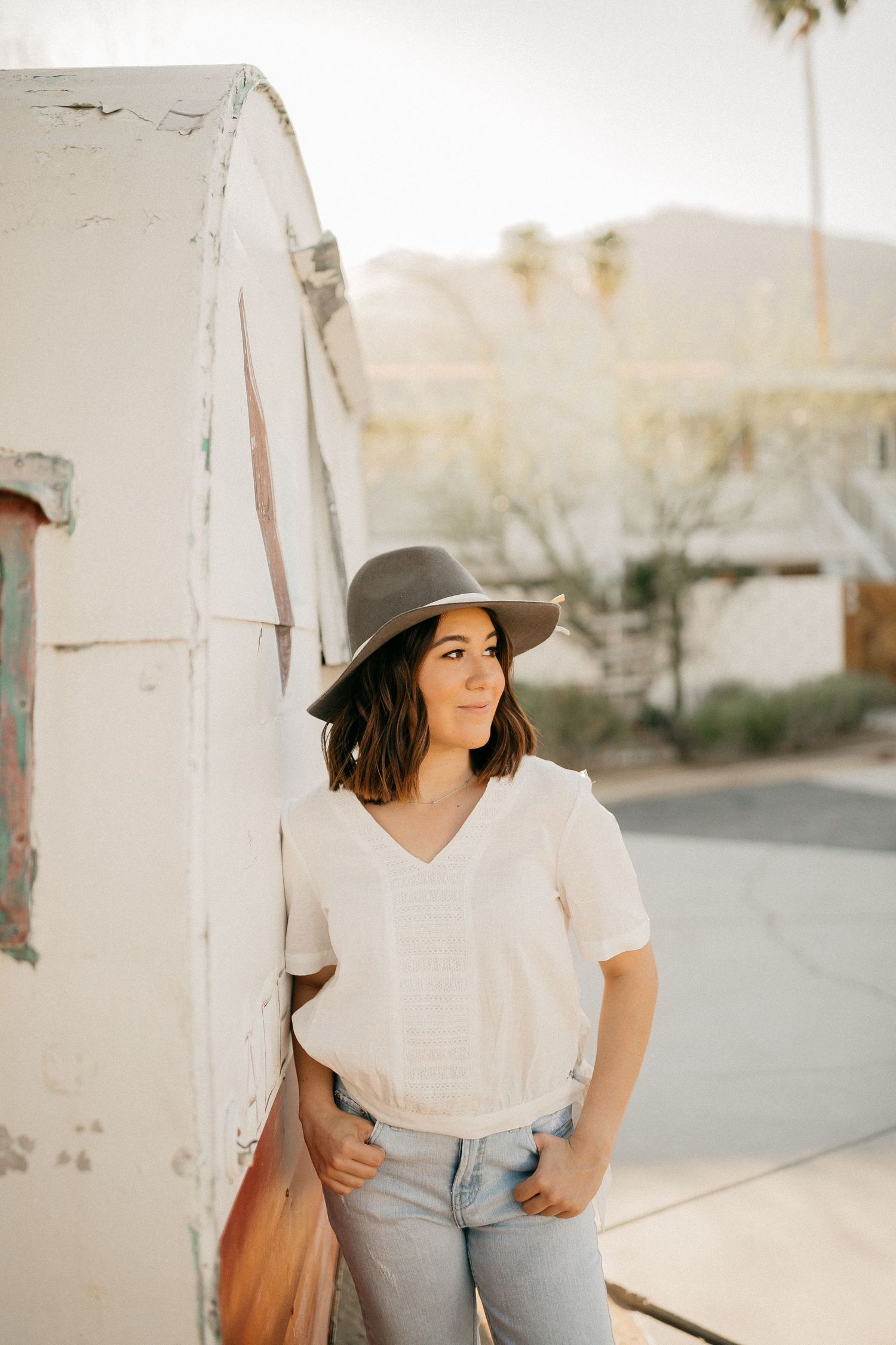 Casual portrait against white wall wearing hat, white shirt and jeans in desert setting.