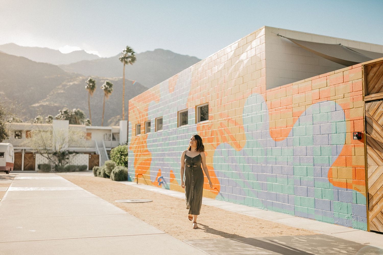 Person walking past colorful painted mural wall with mountains visible in background.