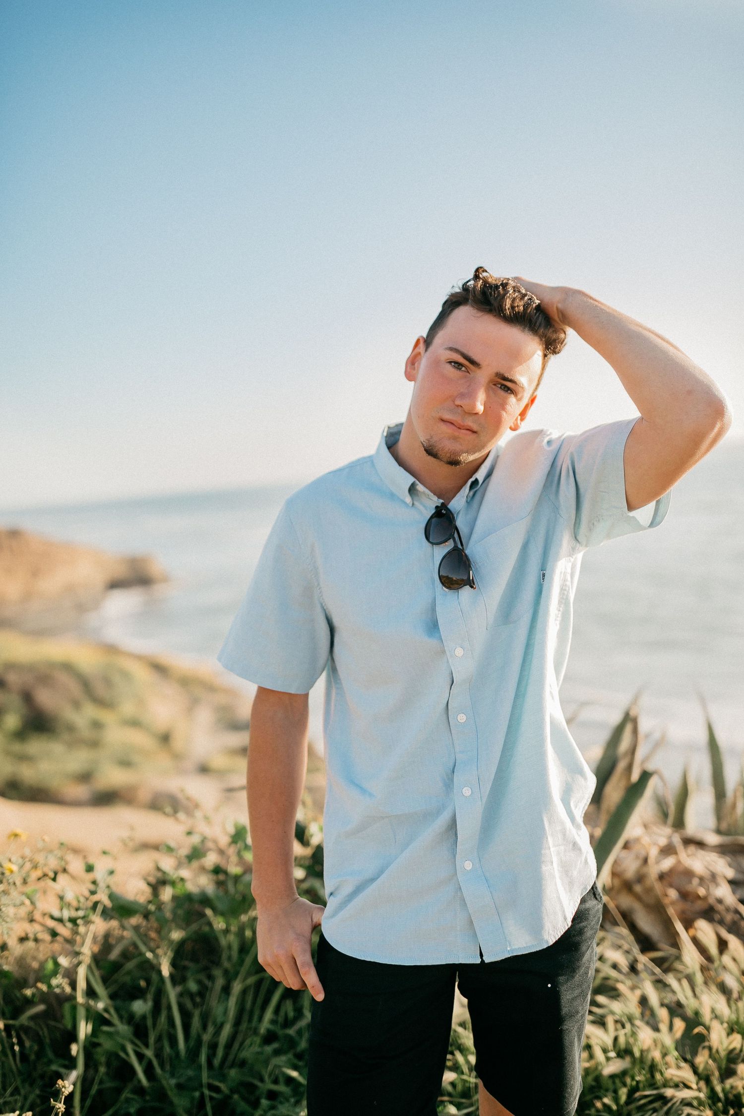 Casual portrait of man in white shirt standing on coastal cliff with ocean view.