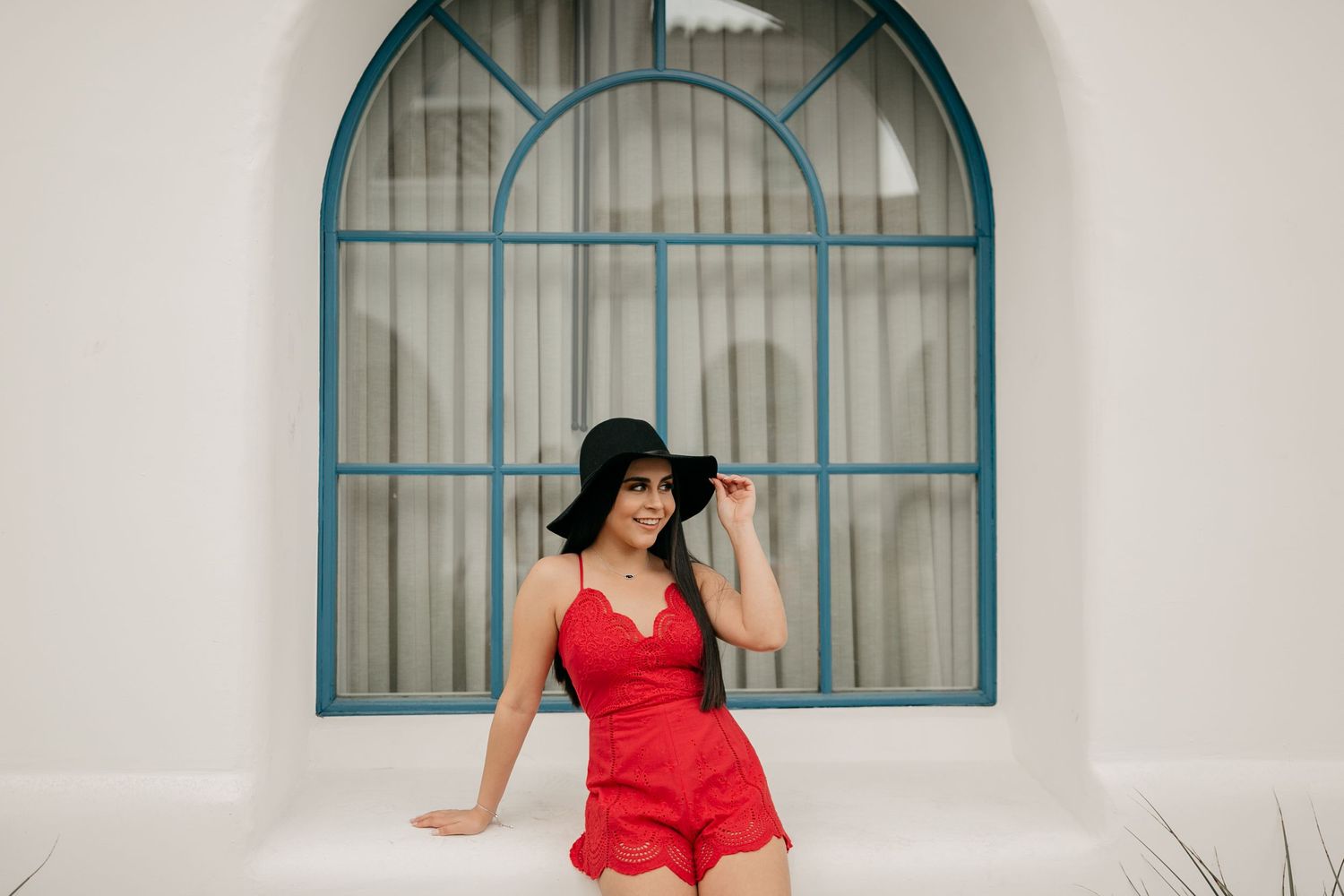 Portrait in red romper against white wall with decorative blue-framed window.