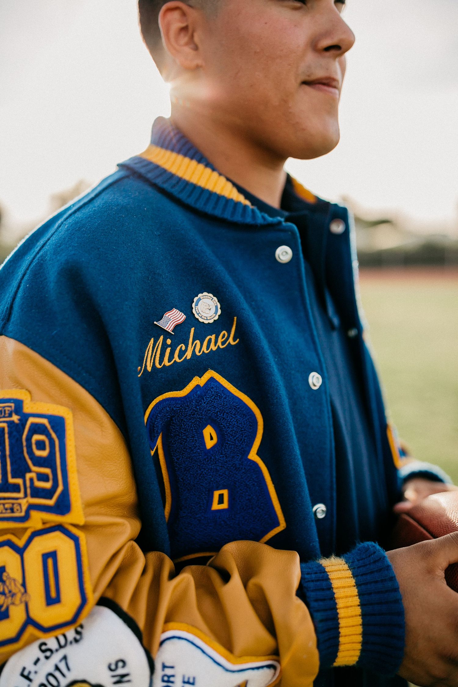 Navy and gold letterman jacket with embroidered patches and name detail.