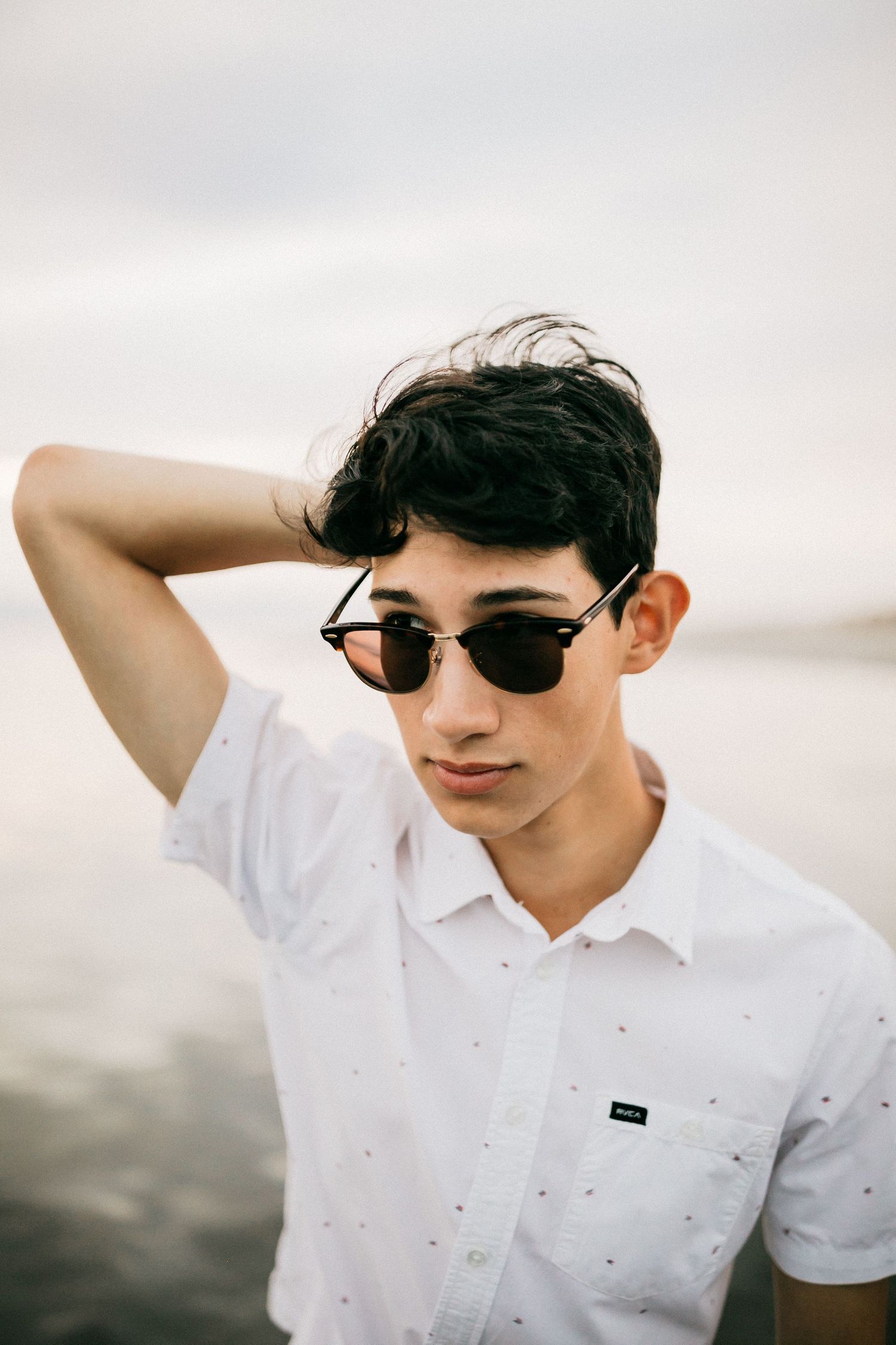 Stylish casual summer outfit with sunglasses against a serene beach backdrop.