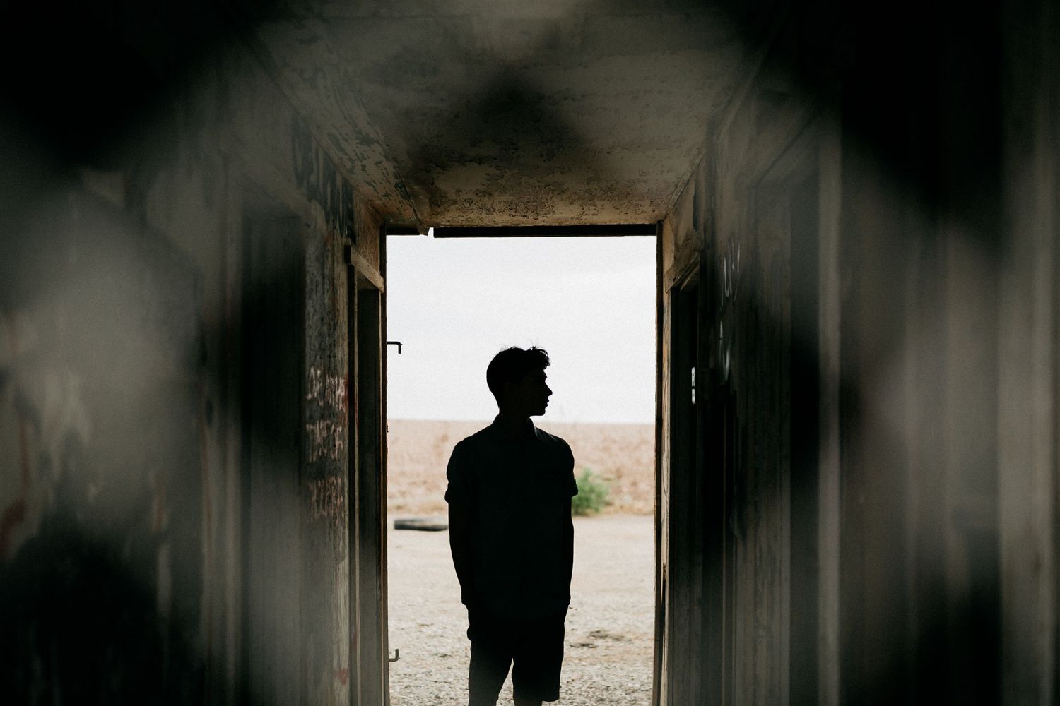 Silhouette of a person standing in a doorway framing a bright desert landscape.