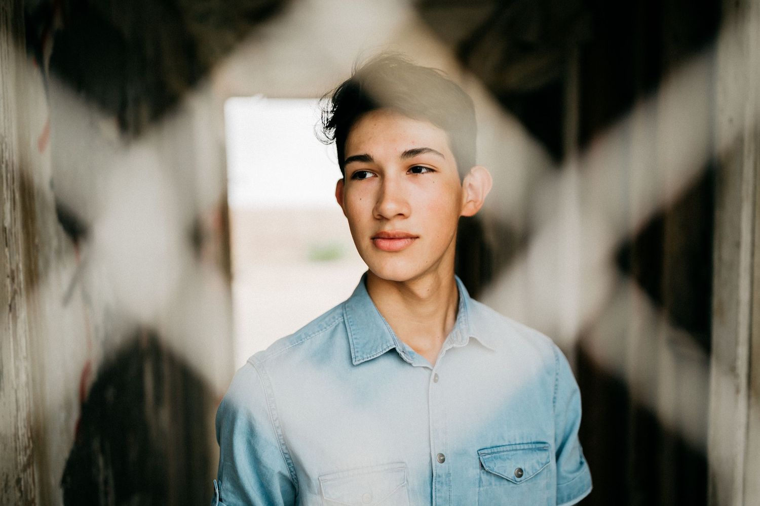 Portrait through geometric window frame showing light denim shirt styling.