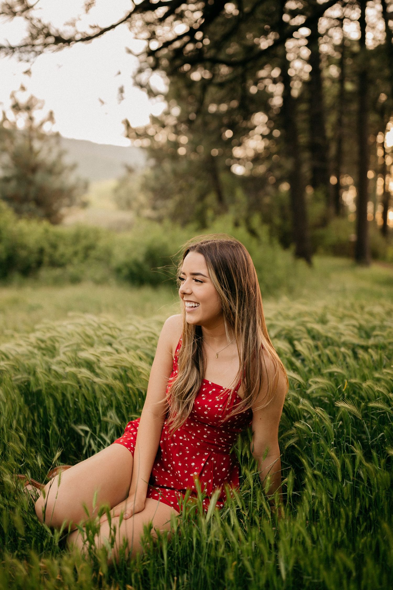 Woman in red polka dot dress sitting in a field of tall grass during golden hour sunset.