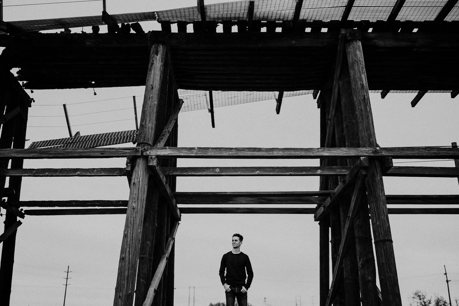 Dramatic black and white silhouette of a person standing under wooden beams against bright sky.