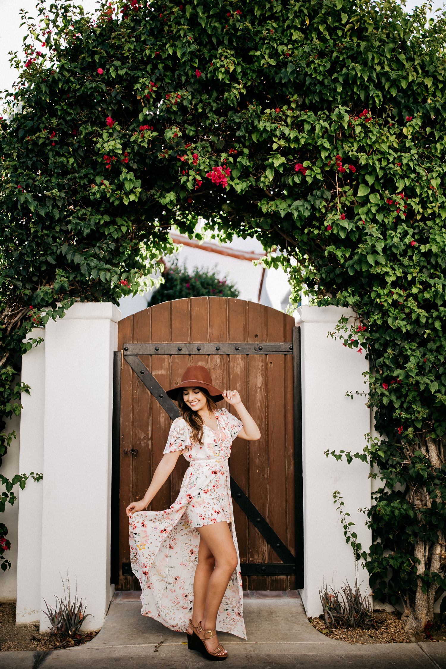 A floral-draped wooden doorway with a person in a flowing summer dress posing beneath.