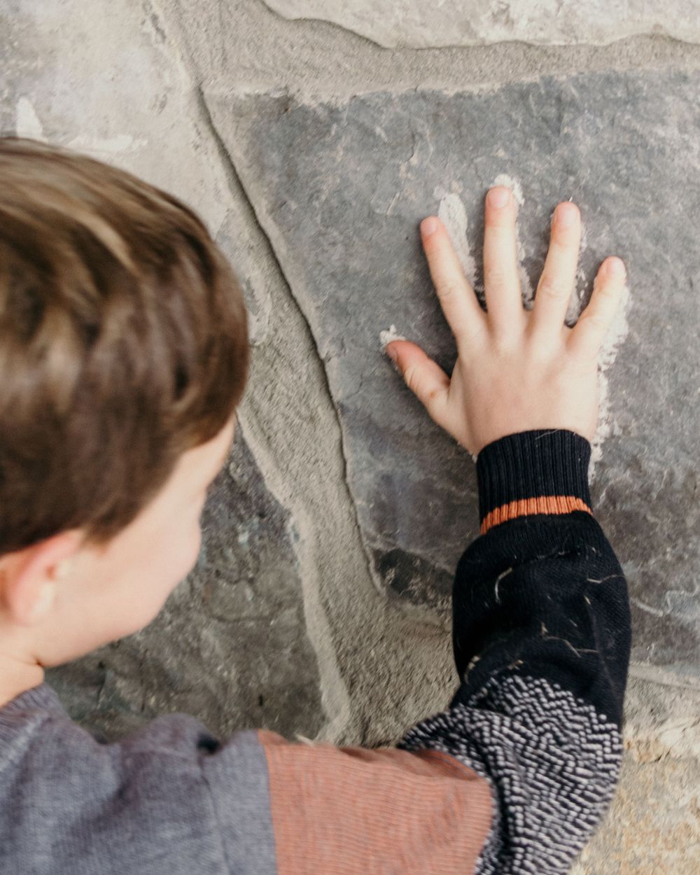 Close-up of a child's hand touching a textured stone wall.
little boy, family photography