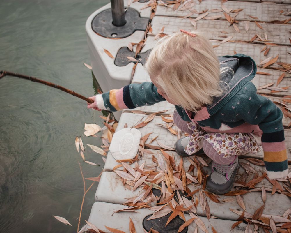 Child in winter clothes looking down at fall leaves on a deck.