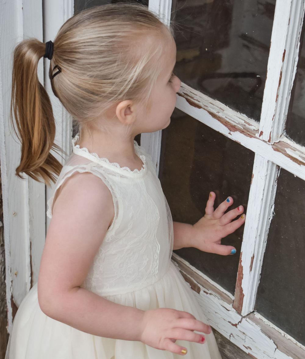 A person in a cream dress looks through an old white window frame.