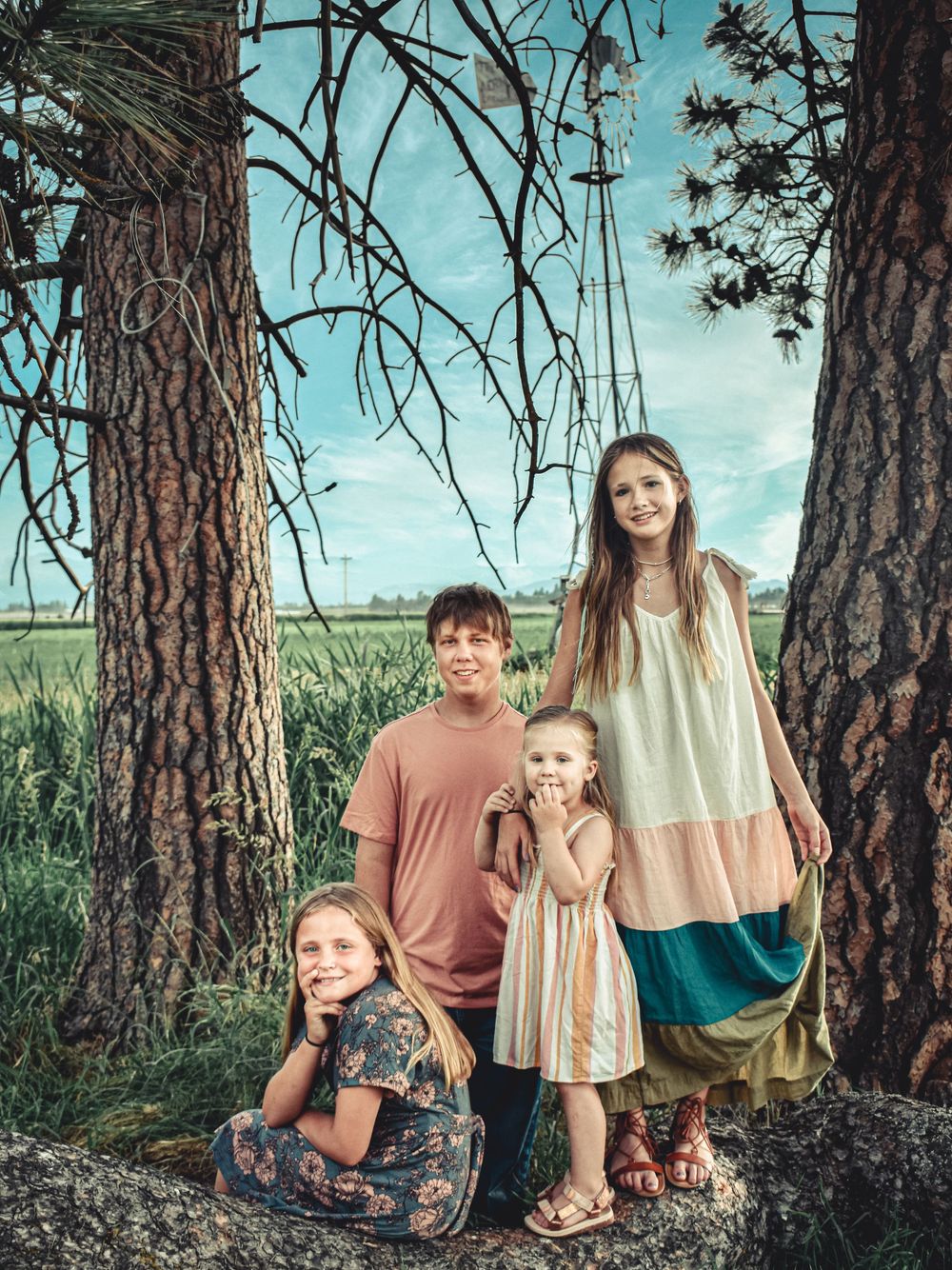 Family group poses between tall pine trees against blue sky.