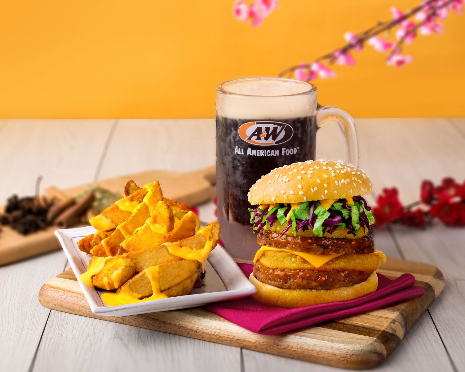 Juicy hamburger with french fries and dark beer served on wooden board against orange background.
