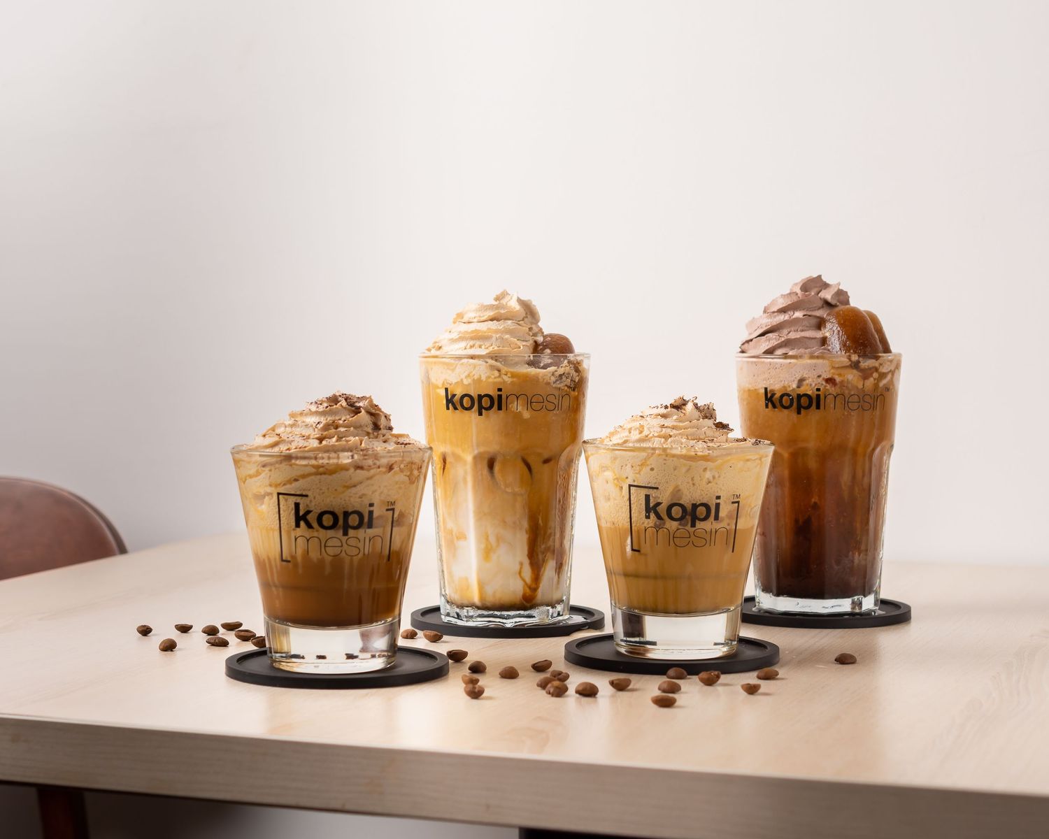Row of coffee drinks with whipped cream toppings in Kopi branded cups.