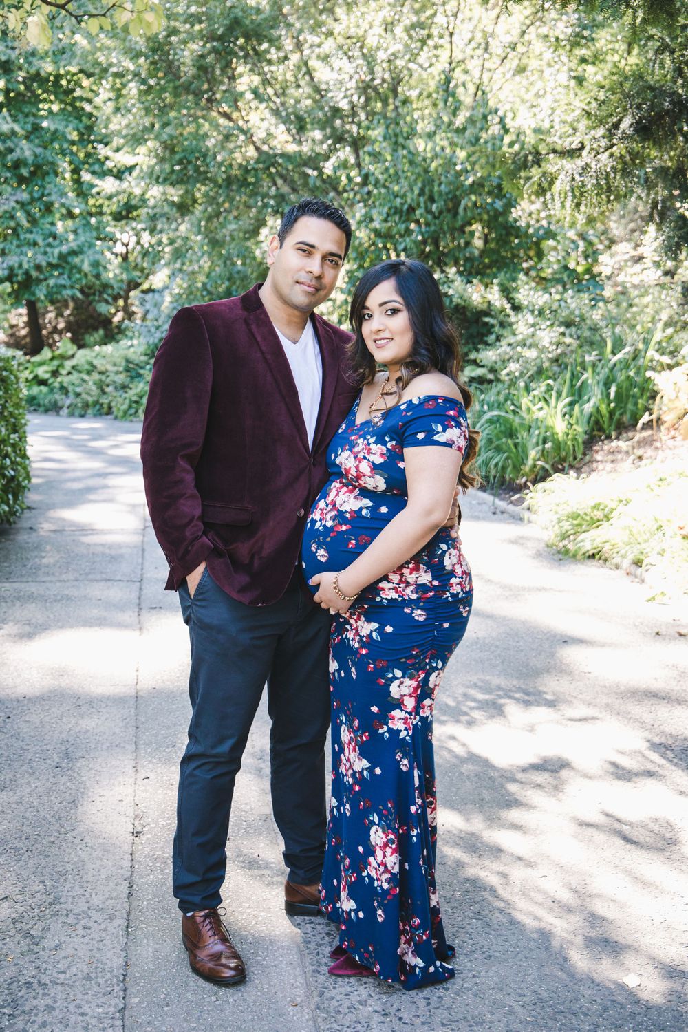 A couple poses on a garden path, wearing burgundy and blue floral formal wear.