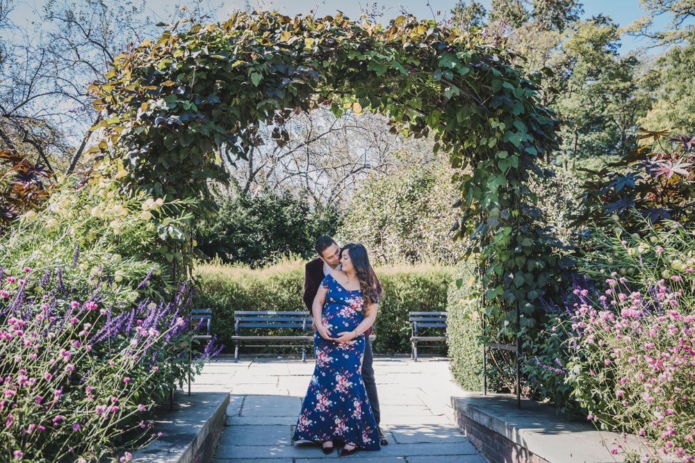 A floral dress stands beneath an elegant garden archway covered in climbing vines and purple flowers.