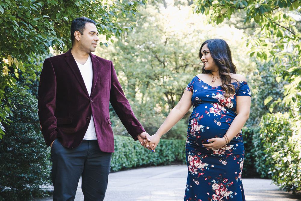A couple holds hands while walking along a garden path, wearing burgundy and blue floral attire.
