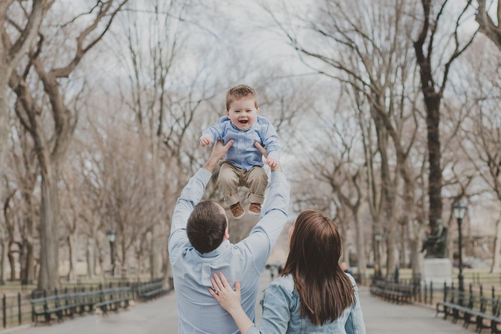 Family enjoying playful moments together in a park with bare trees.