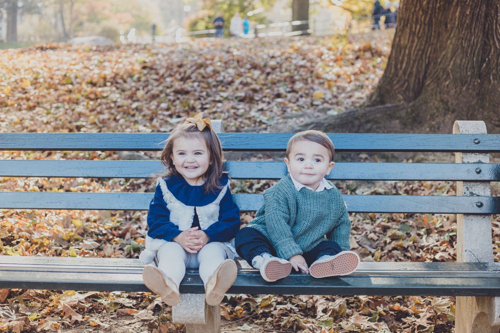 Children sitting together on park bench surrounded by autumn leaves.