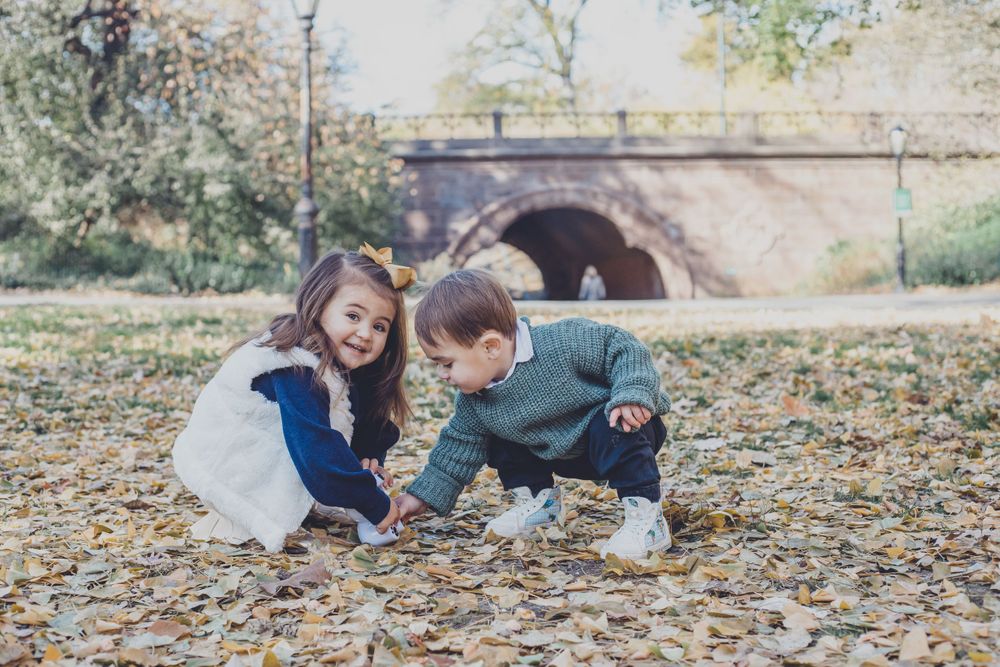 Children playing in fallen autumn leaves during outdoor photo session.
