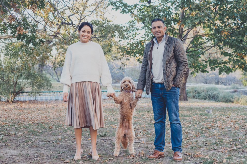A couple and their dog enjoy a fall day outdoors among trees with changing leaves.